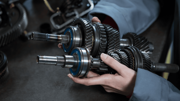 Engenheiro segurando conjunto mecânico com diferentes tipos de engrenagens metálicas helicoidais e cilíndricas usadas em sistemas de transmissão industrial.