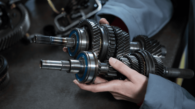 Engenheiro segurando conjunto mecânico com diferentes tipos de engrenagens metálicas helicoidais e cilíndricas usadas em sistemas de transmissão industrial.