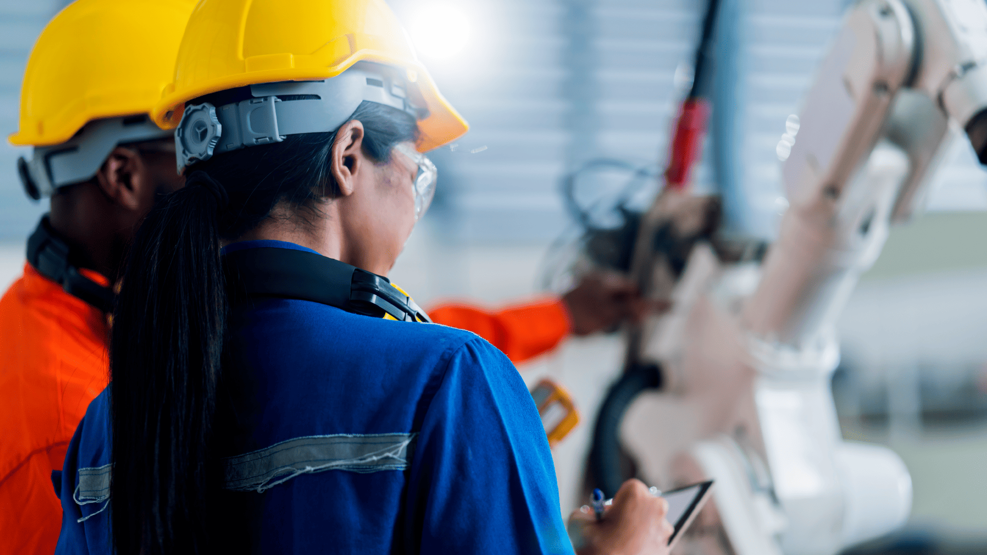 Técnicos analisam e realizam manutenção em braço robótico em ambiente de automação industrial, utilizando tablet para monitoramento de dados.