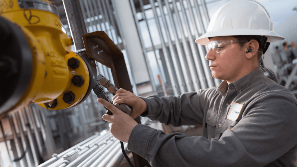 Técnico industrial utilizando um dispositivo de medição portátil em uma flange de tubulação como parte do processo de coleta de dados para diagnósticos em acoplamentos em maquinário pesado.