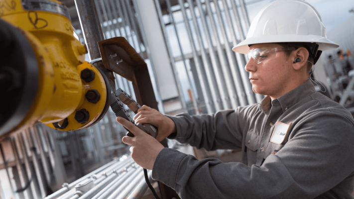 Técnico industrial utilizando um dispositivo de medição portátil em uma flange de tubulação como parte do processo de coleta de dados para diagnósticos em acoplamentos em maquinário pesado.
