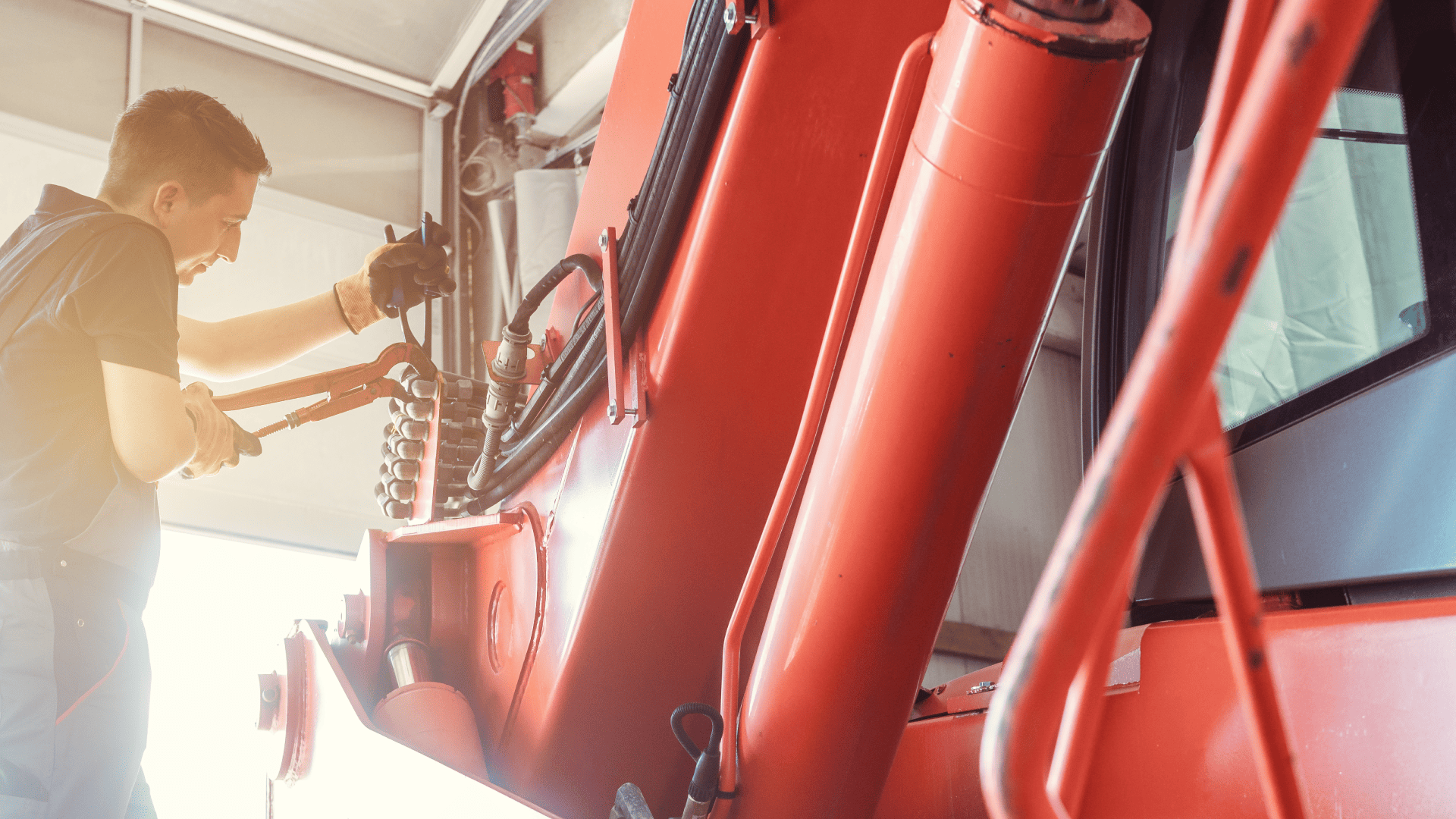 Técnico em uma oficina utiliza uma chave de grifo para ajustar componentes hidráulicos de uma máquina pesada, como parte do processo de manutenção na entressafra.