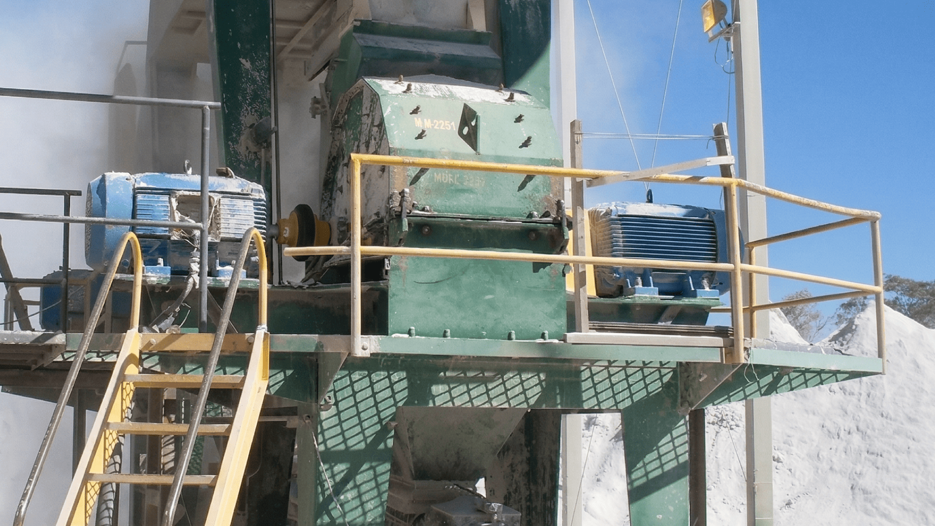 Detalhe de motores azuis em plataforma elevada acionando o mecanismo de britagem, destacando a importância do acoplamento para britador na absorção de vibrações e compensação de desalinhamentos.