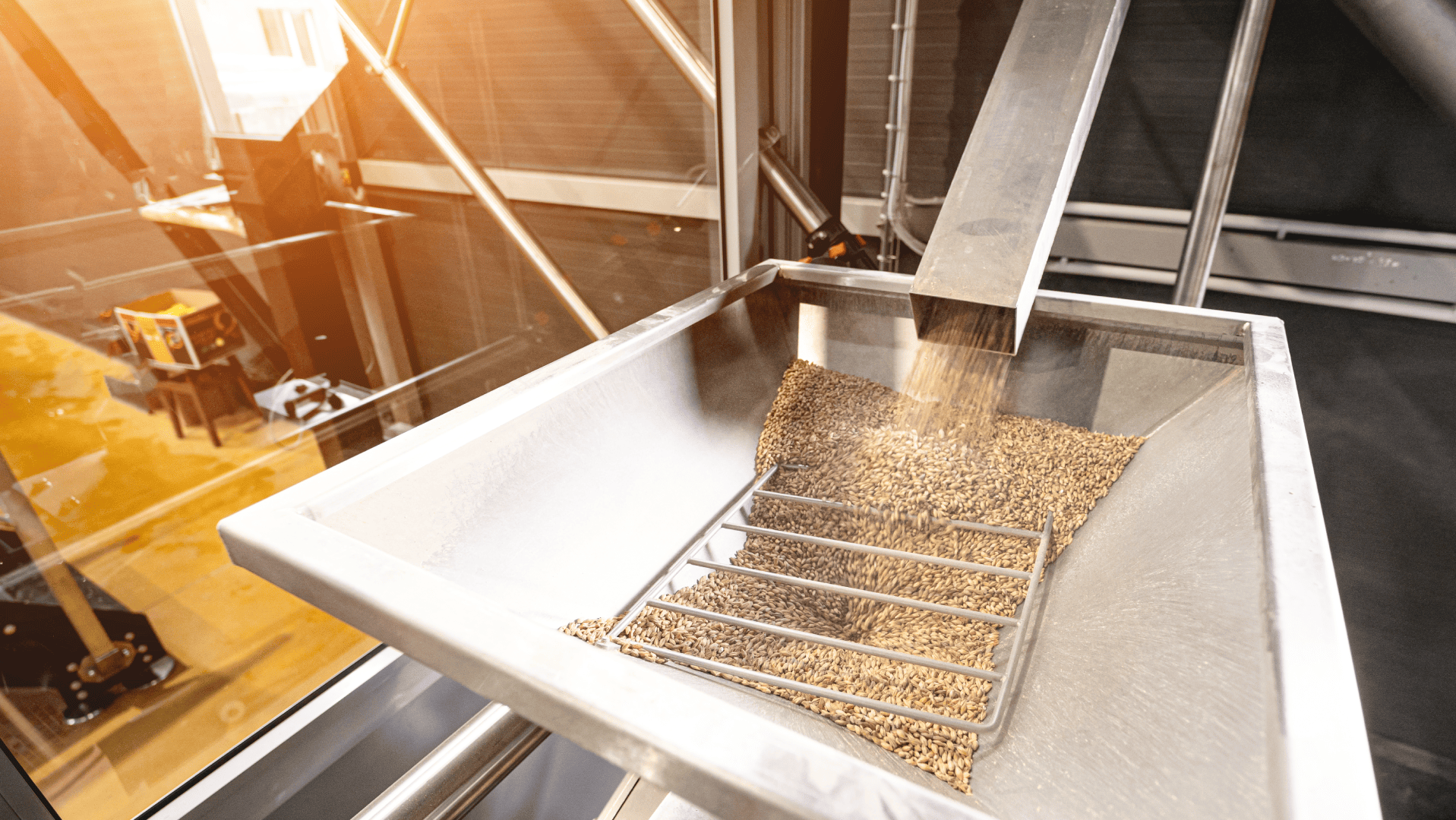 Moega de recepção de grãos de cevada com grade de proteção e iluminação âmbar, como as usadas em processos de moagem. Este ambiente de processamento é ideal para a aplicação de robustos acoplamentos para moinhos.