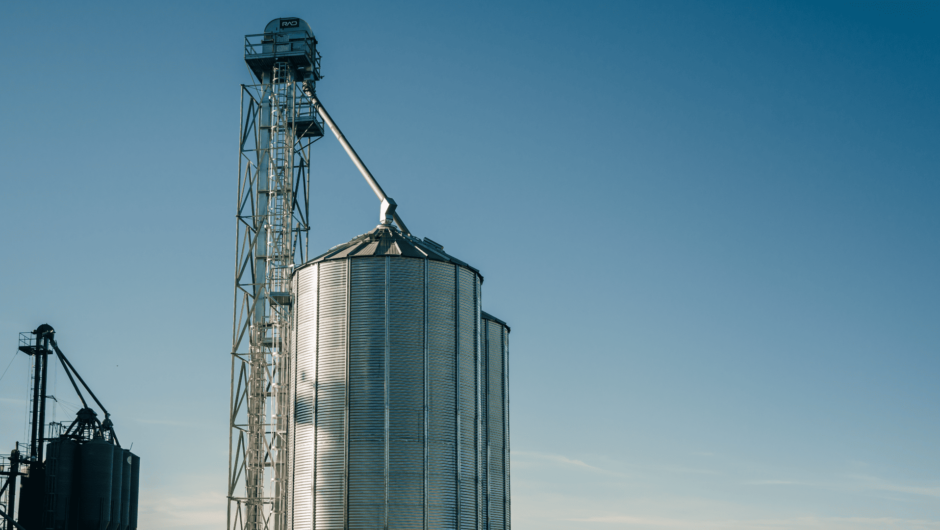 Silo metálico corrugado com torre de elevador de grãos e tubulação de descarga, exemplificando sistemas mecânicos que dependem de acoplamentos para silos agrícolas para a movimentação eficiente da safra.