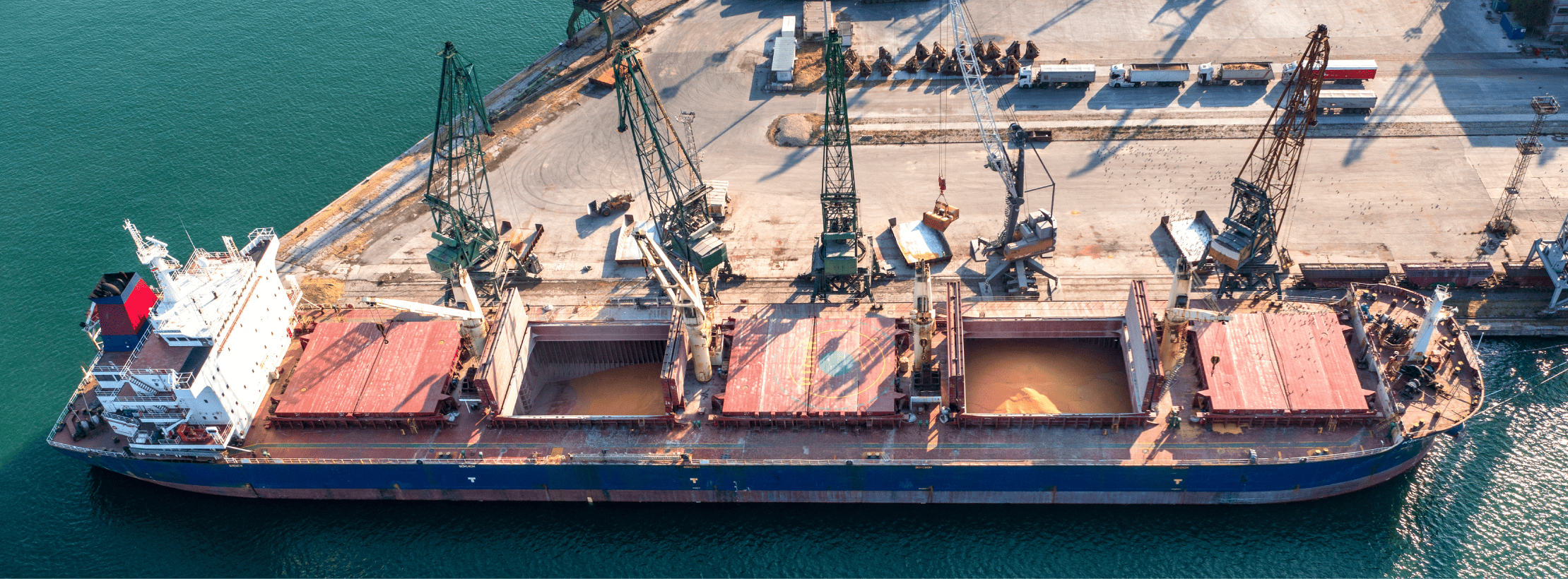 Vista aérea de um navio cargueiro sendo carregado em um terminal portuário, destacando a complexa infraestrutura logística que opera com acoplamentos para equipamentos de transbordo de grande porte.