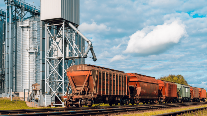 Vagões de trem posicionados para carregamento de grãos sob uma estrutura de silos metálicos, cujo sistema de movimentação de carga exige acoplamentos para equipamentos de transbordo de alta resistência.