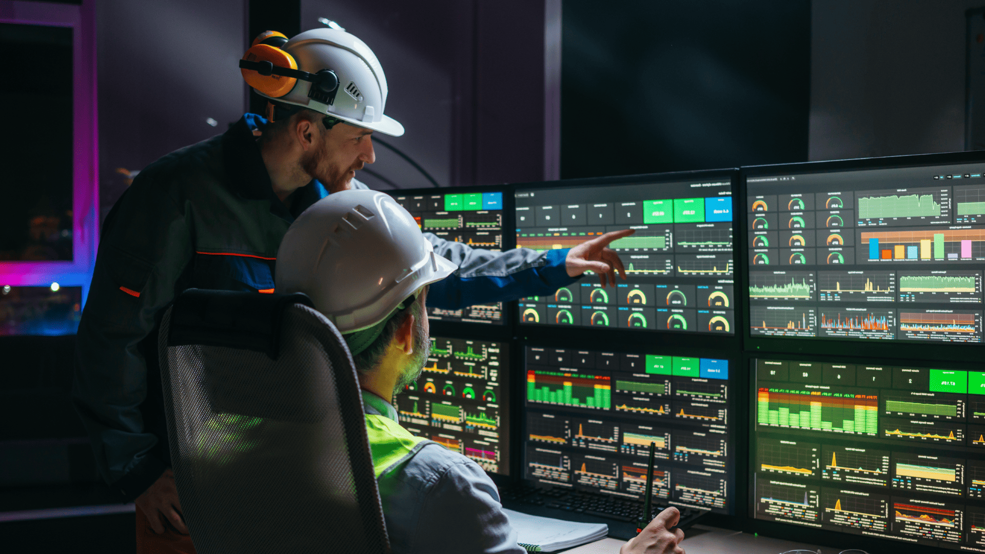 Engenheiros em uma sala de controle analisam múltiplos monitores com gráficos e painéis em tempo real, gerenciando processos industriais integrados por uma rede IIoT.