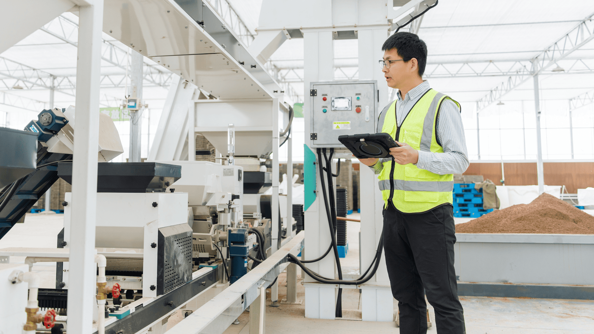 Engenheiro industrial de colete refletivo usa um tablet para monitorar dados transmitidos por sensores industriais em uma máquina automatizada de processamento em uma fábrica moderna.