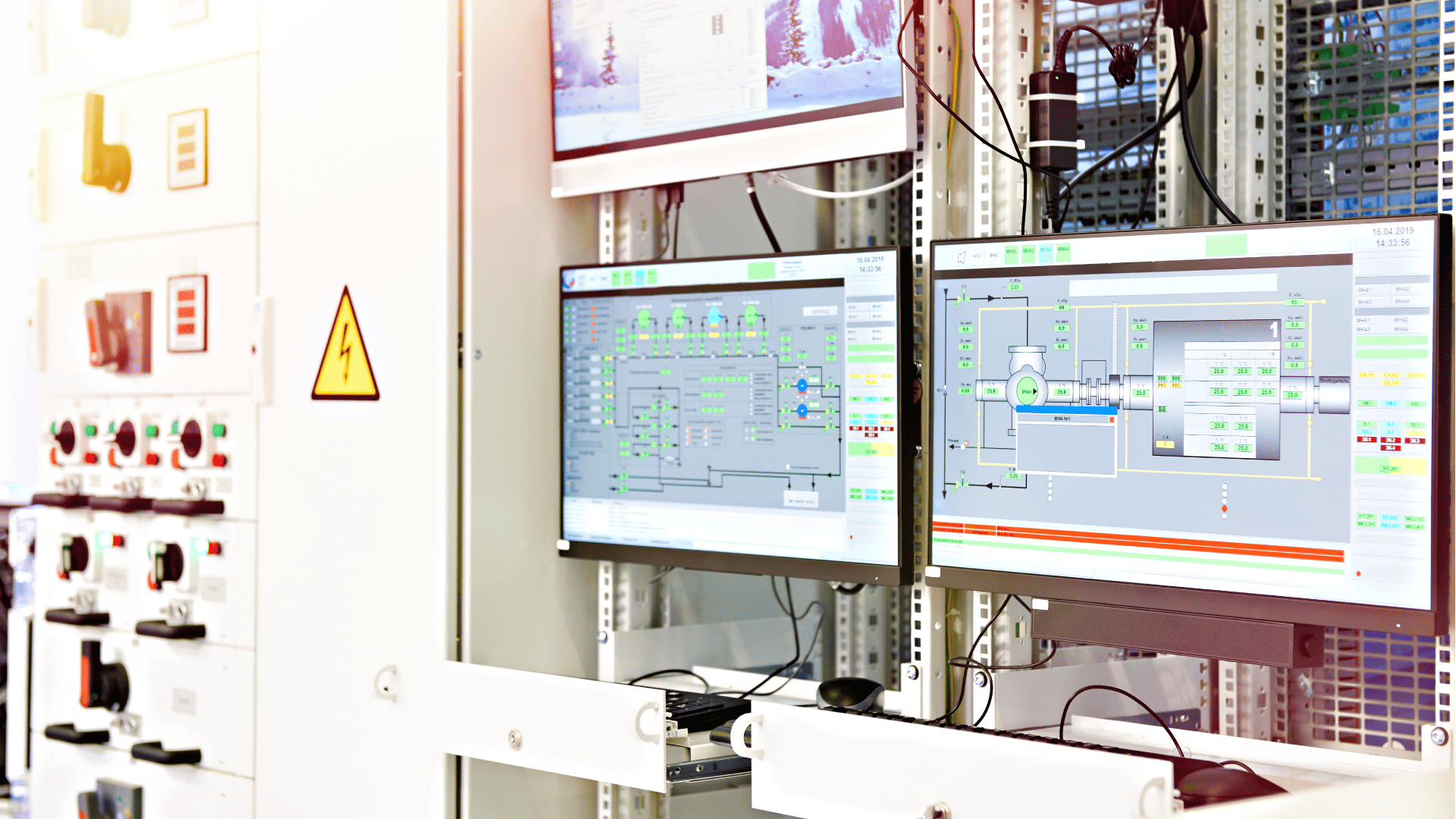 Um close-up de um painel de controle industrial e monitores de computador em uma sala de controle, exibindo diagramas técnicos que visualizam dados em tempo real coletados por sensores industriais espalhados pela planta.