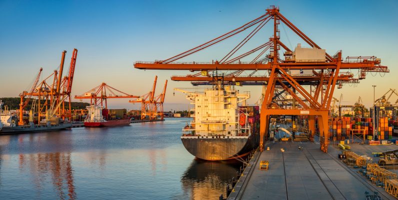Vista panorâmica ao amanhecer de um complexo e automated terminal de contêineres, destacando um gigantesco guindaste de pórtico STS (Ship-to-Shore) em operação sobre um navio porta-contêineres, exemplificando acionamentos críticos em operações portuárias de alta capacidade e os complexos elementos de transmissão necessários para sua operação confiável.